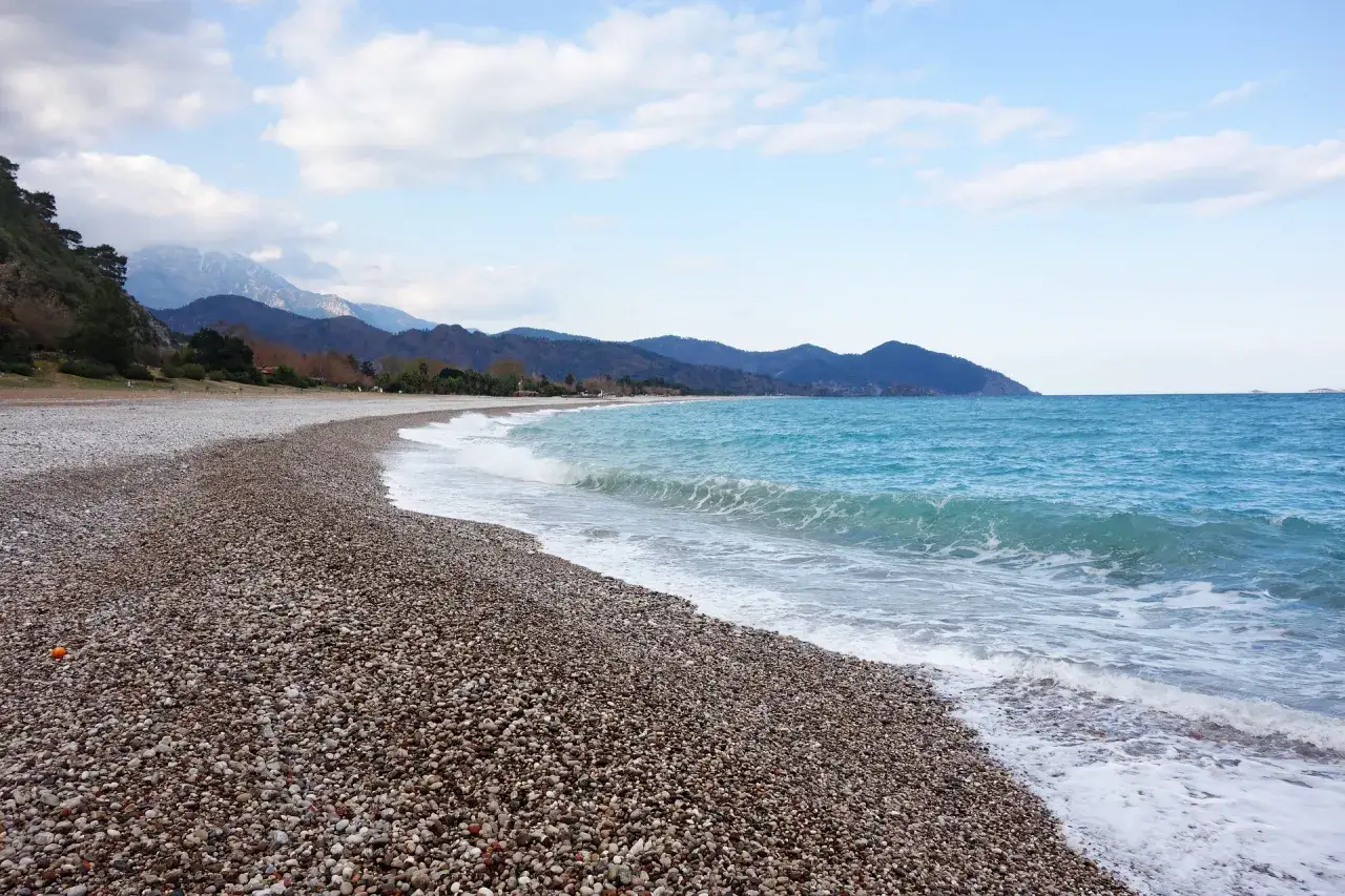 Kamienista plaża i turkusowe morze. Czy Antalya jest bezpieczna? Spokojne fale i góry w tle tworzą idylliczny krajobraz.