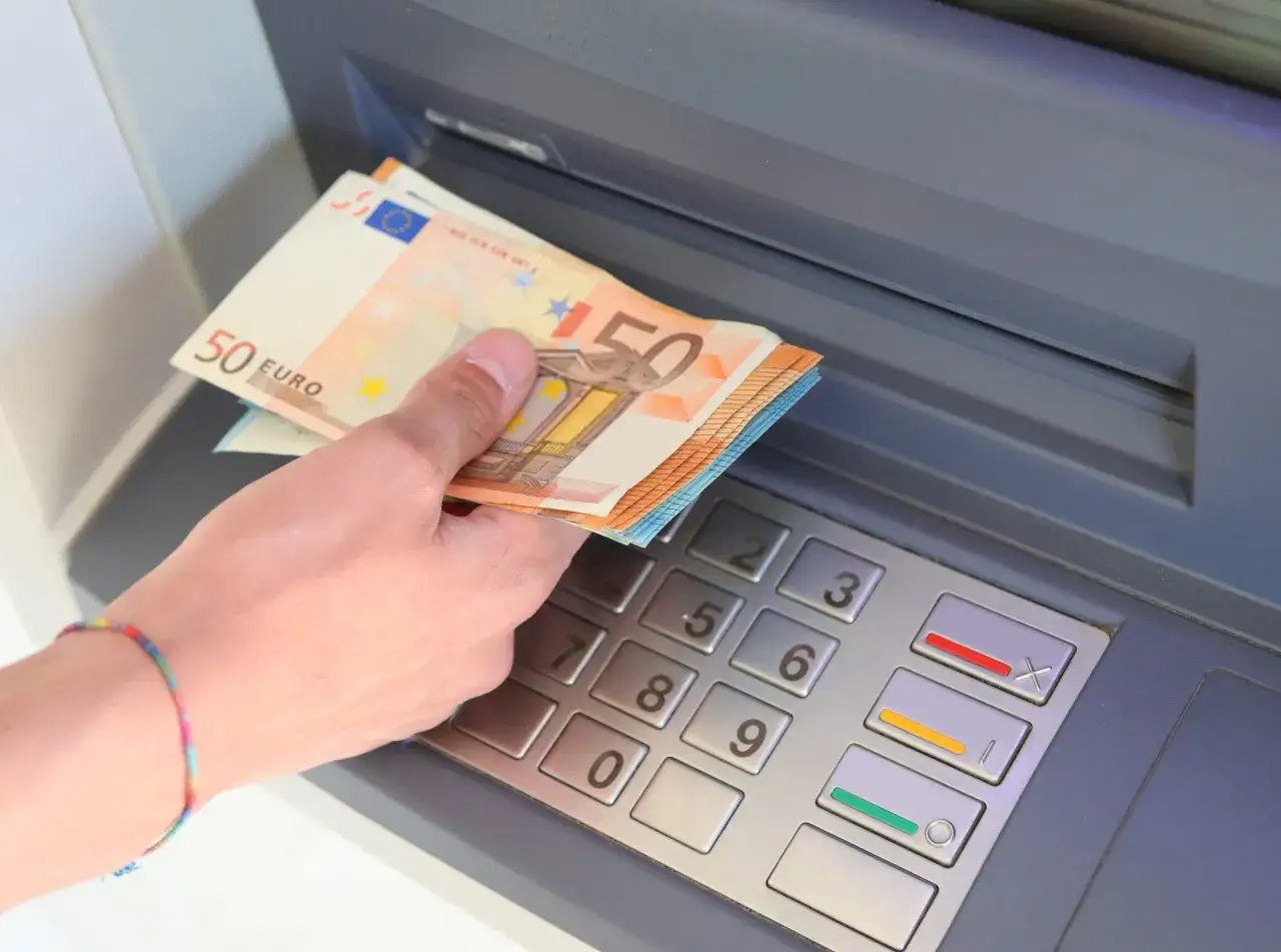 Dłoń trzyma banknoty 50 euro przy bankomacie. W Hiszpanii, podobnie jak w wielu krajach UE, jaką walutą płaci się w Hiszpanii? Euro.