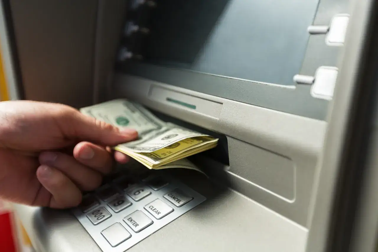 Dłoń wyciąga banknoty z bankomatu. Planując podróż, zastanawiasz się, jaką walutę zabrać do Brazylii?
