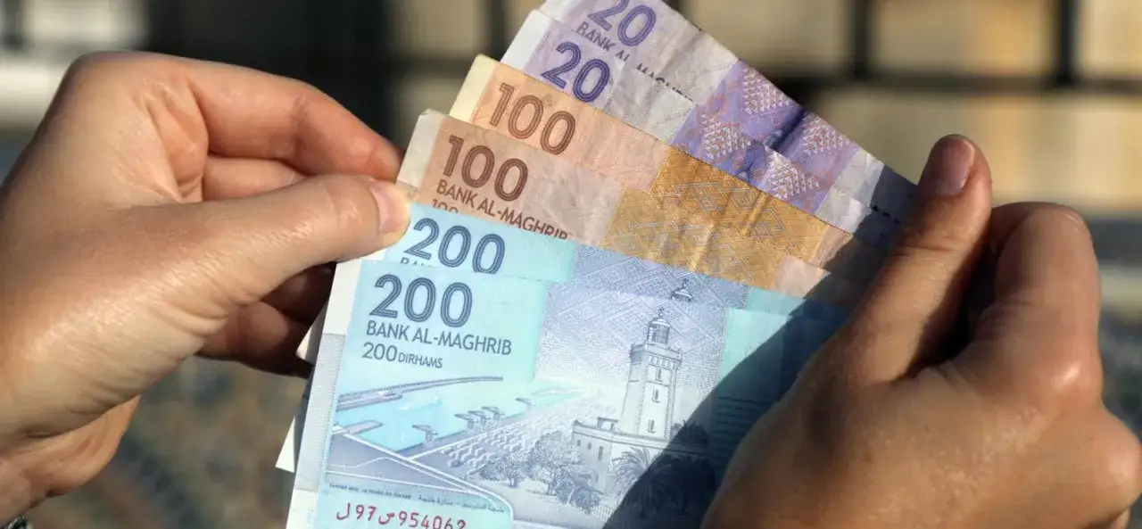 Ręka trzyma marokańskie dirhamy. Planujesz podróż i zastanawiasz się, jaką walutę zabrać do Maroka? Dirhamy to lokalna waluta.