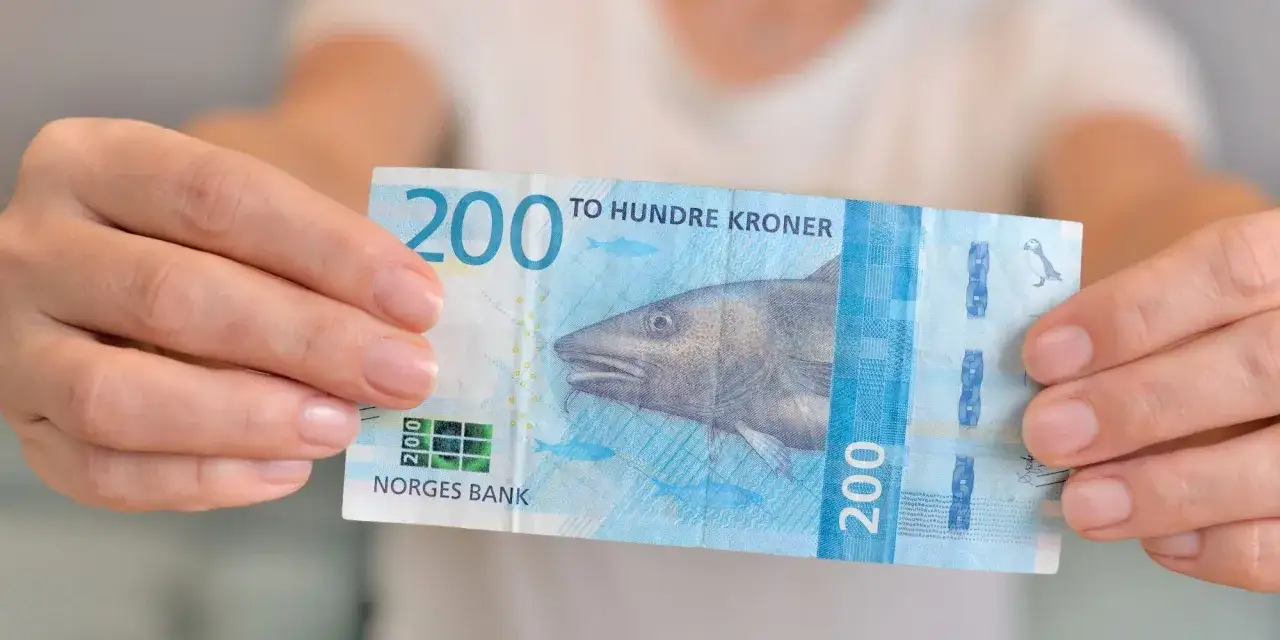 Dwie ręce trzymają banknot 200 koron norweskich z dorszem. To waluta kr.