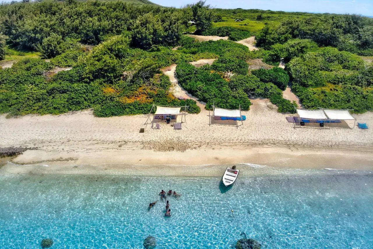 Idealny dzień na Mauritiusie: ludzie kąpią się w krystalicznie czystej wodzie, łódź przy brzegu, a na plaży zacienione miejsca.