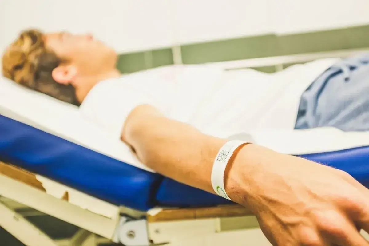 Chłopak leży na łóżku, a na jego ręce opaska identyfikacyjna. Kolory opasek na rękę w szpitalu mają znaczenie.