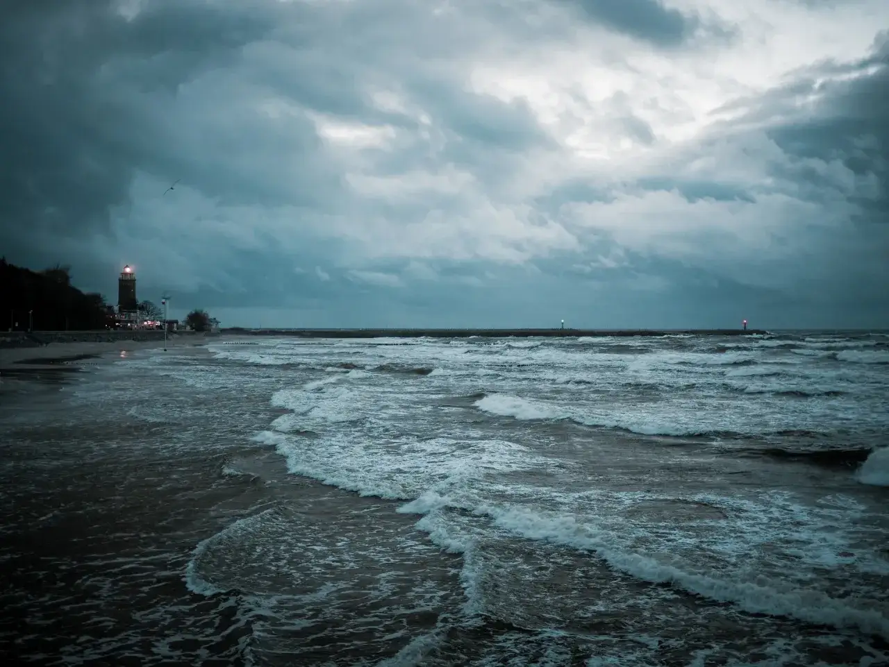 Mroczne, burzowe niebo nad Bałtykiem. Fale rozbijają się o brzeg, a latarnia morska oświetla drogę. W takie dni czuć, kiedy jest najwięcej jodu nad morzem.