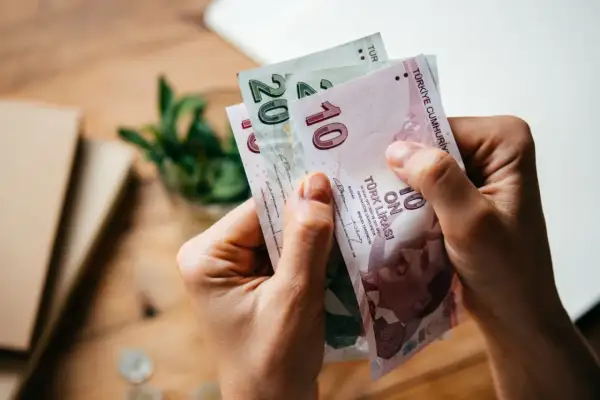 Ręce trzymają banknoty 10 i 20 lir tureckich. Planujesz podróż i zastanawiasz się, jaką walutę zabrać do Turcji? Lira turecka to odpowiedź!