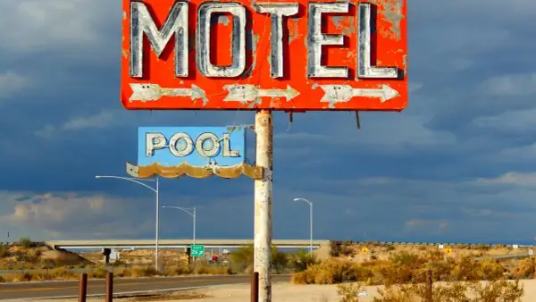 Stary, zniszczony neonowy szyld "MOTEL" i "POOL" na tle burzowego nieba. Obok droga i most.