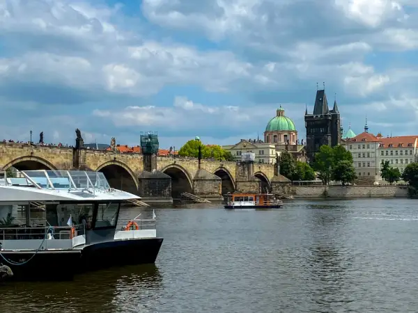 Widok na Most Karola w Pradze, z łodziami na Wełtawie. Turyści zastanawiają się, czy w Pradze można płacić euro, ale czeska korona jest walutą.