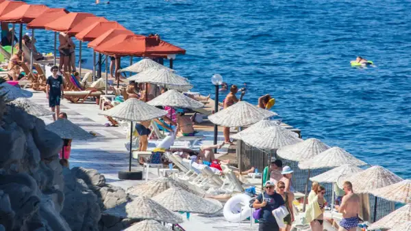 Ludzie odpoczywają na plaży pod parasolami, w tle widać turkusowe morze.
