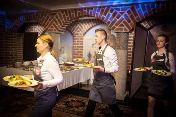 Kelnerzy niosą talerze z jedzeniem. Zastanawiasz się, jak się ubrać na kolację all inclusive? Elegancko, ale wygodnie, jak obsługa.