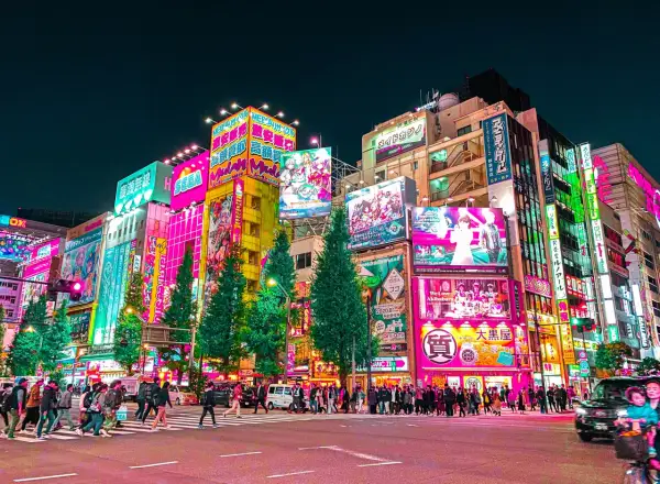 Akihabara nocą, pełna neonów i reklam, to miejsce, co warto zobaczyć w Tokio. Tłumy ludzi przechodzą przez pasy.